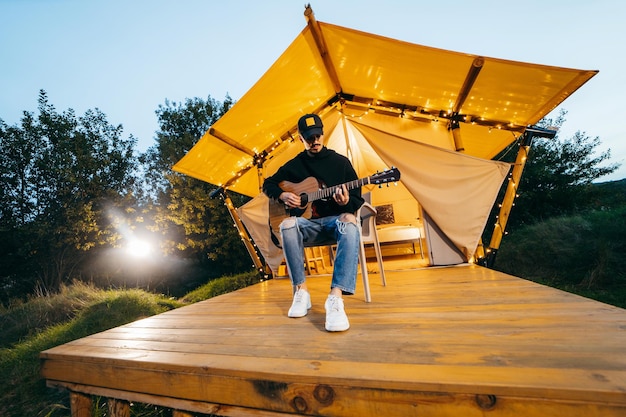 Young guy playing acoustic guitar in nature at evening