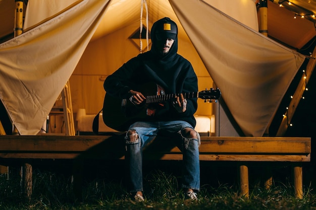 Young guy playing acoustic guitar in nature at evening