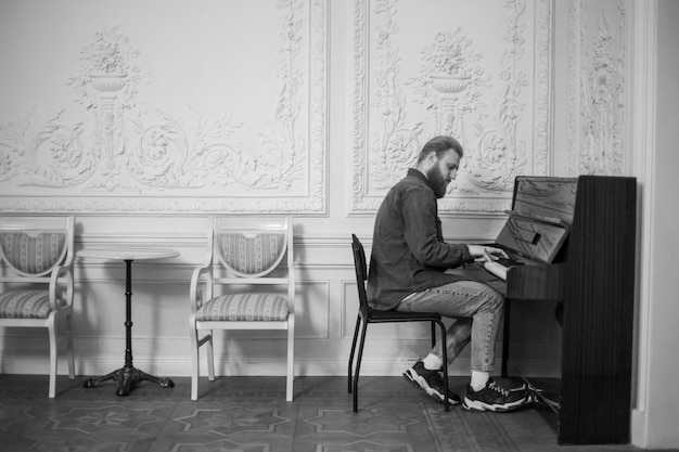Молодой парень играет на пианино в большом белом зале черно-белого цвета