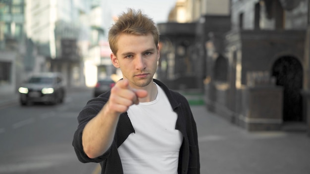 Young guy pointing finger looking at the camera city road\
background