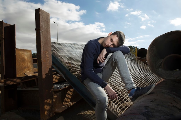 Photo young guy posing in an industrial area against the backdrop of colored and rusty iron structures