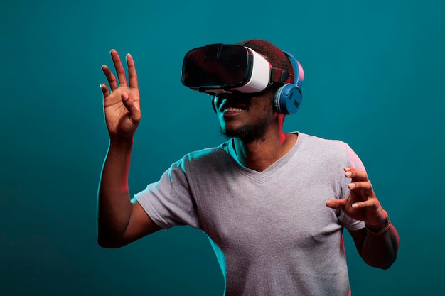 Young guy raising hands to play futuristic game with vr glasses, advertising interactive 3d simulation on goggles technology. Millennial person enjoying virtual reality headset experience.