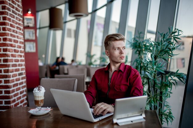 Young guy in shirt works on laptop while sitting at table in cafeteria