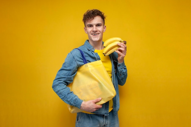 Young guy shopper with fabric eco bag holds bananas and puts them in reusable nonplastic bag