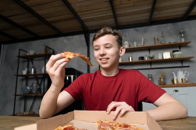 Young guy smiling looking at the piece of pizza he is holding in his hand