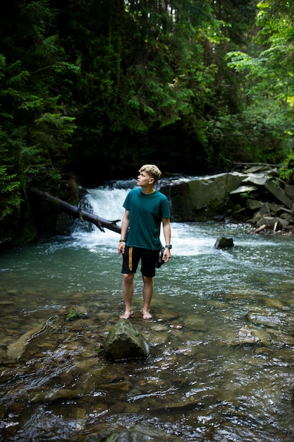 Молодой парень стоит у реки на фоне водопада