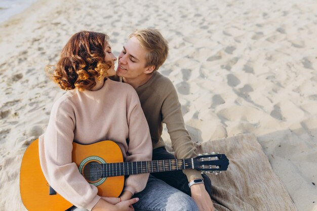 Young guy teaching his girlfriend how to play guitar selftaught\
couple in love having fun on the beach hugging and kissing