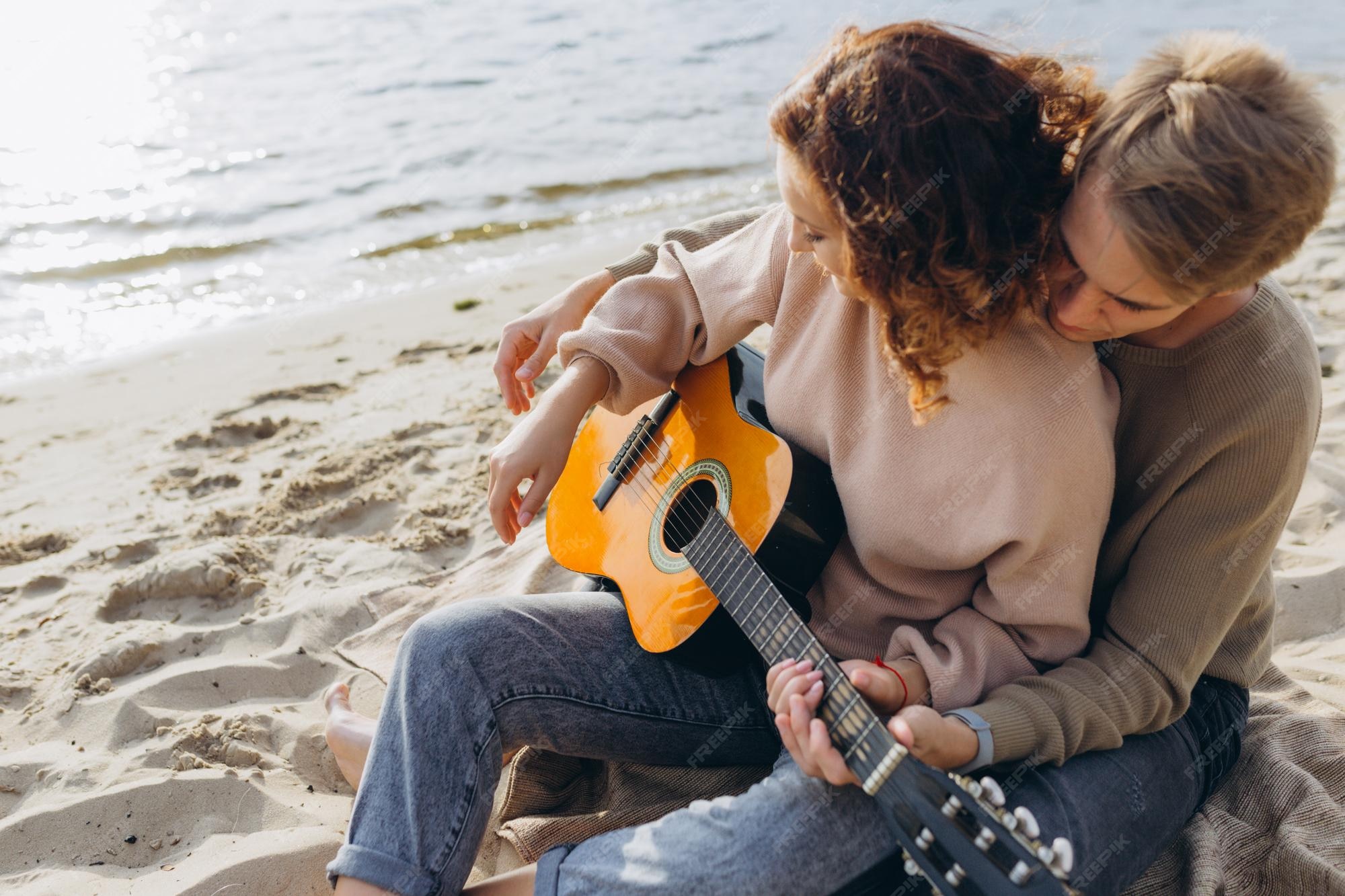 Premium Photo | Young guy teaching his girlfriend how to play guitar selftaught couple in love having fun on the beach