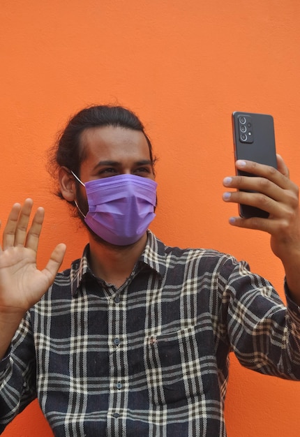 Photo a young guy wearing face mask saying hello with waving his hand to someone while video call