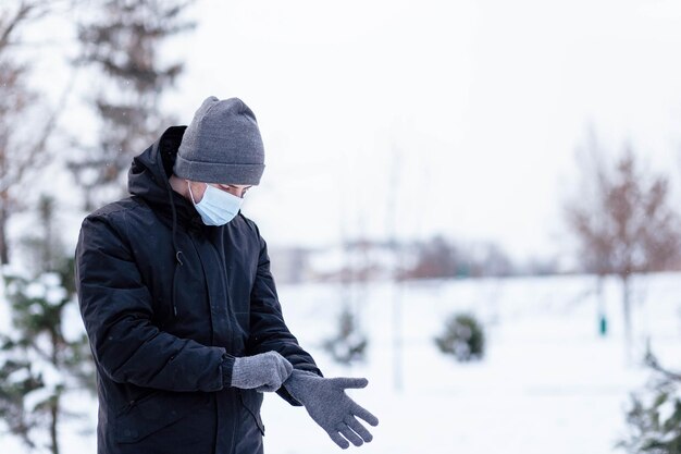 A young guy in winter wears a mask Young man in protective antiviral mask on the street The guy in winter clothes in a protective mask Young man in warm clothes and scarf on a winter day