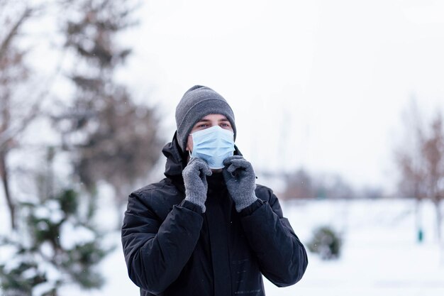 겨울에 젊은 남자가 마스크를 쓰고 거리에서 보호용 항바이러스 마스크를 쓴 청년 보호 마스크를 쓴 겨울 옷을 입은 남자 겨울 날 따뜻한 옷과 스카프를 입은 청년