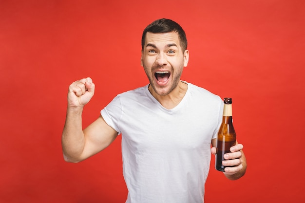 赤い背景で隔離のひげを持つ若い男は、ビールのボトルを保持します。