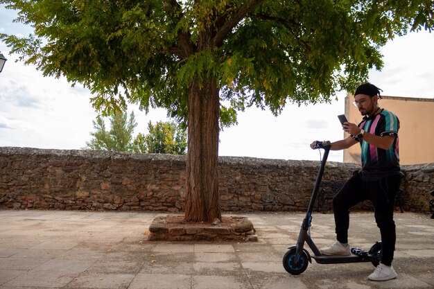 Young guy with braid beard and glasses with mobile on electric scooter