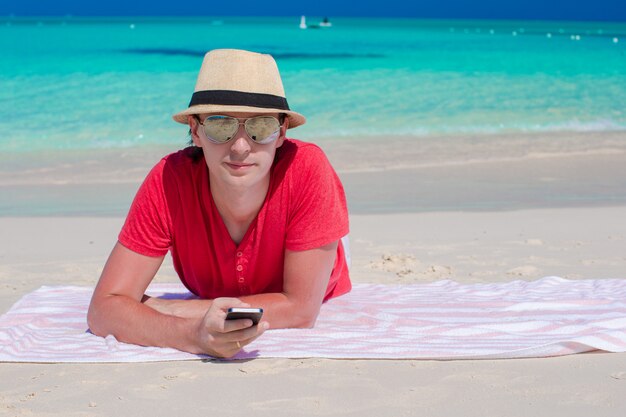 Young guy with cellphone on tropical white beach