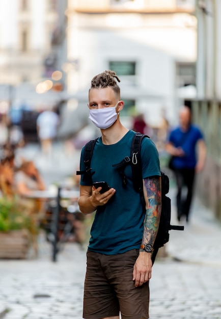 Young guy with face mask and dreadlocks is using mobile phone on the street