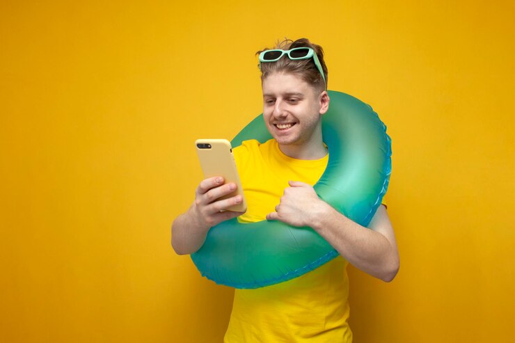 Photo young guy with an inflatable swim ring on vacation in the summer uses smartphone and smiles