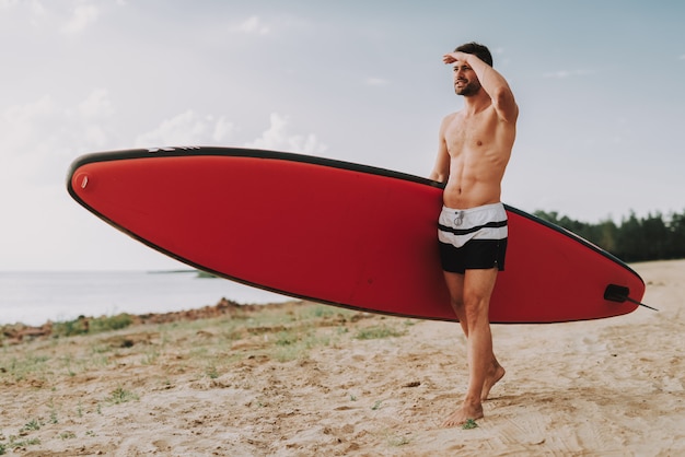 Giovane ragazzo con surf in piedi sulla spiaggia.