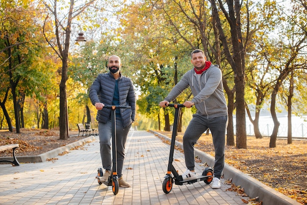 暖かい秋の日に、若い男たちが電動スクーターに乗って公園に乗ります。公園で散歩する。