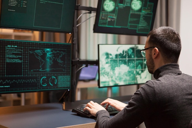 複数の画面を持つコンピューターで危険なウイルスを書いている眼鏡をかけた若いハッカー。
