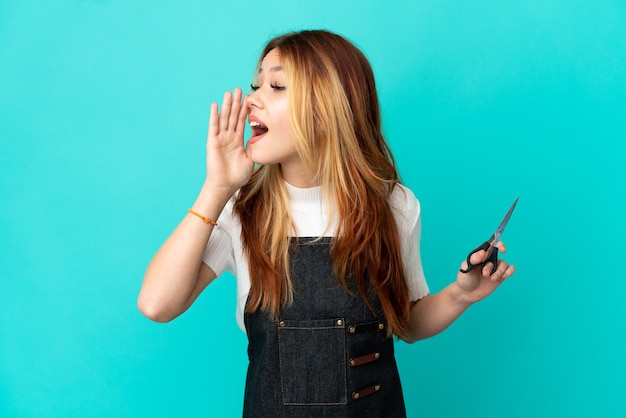 Молодая девушка парикмахер на изолированном синем фоне кричит с широко открытым ртом в сторону