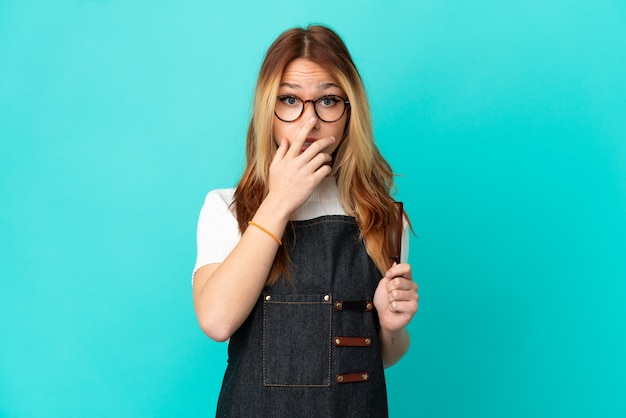 Young hairdresser girl over isolated blue background surprised and shocked while looking right