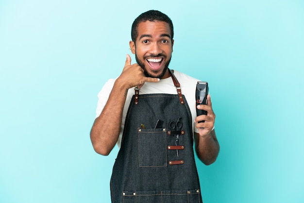 Young hairdresser latin man isolated on blue background making phone gesture. Call me back sign