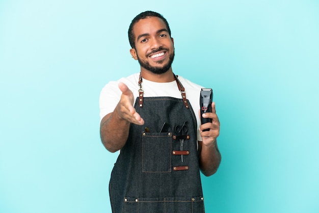 Young hairdresser latin man isolated on blue background shaking hands for closing a good deal