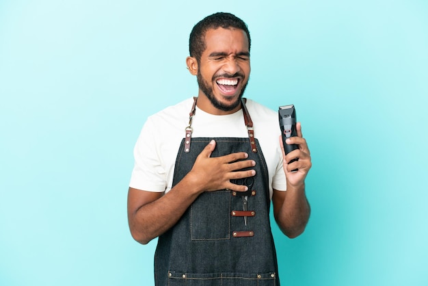 Young hairdresser latin man isolated on blue background smiling a lot