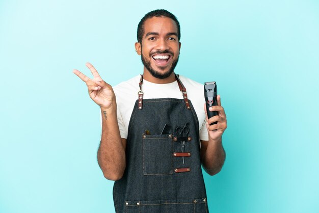 Young hairdresser latin man isolated on blue background smiling and showing victory sign