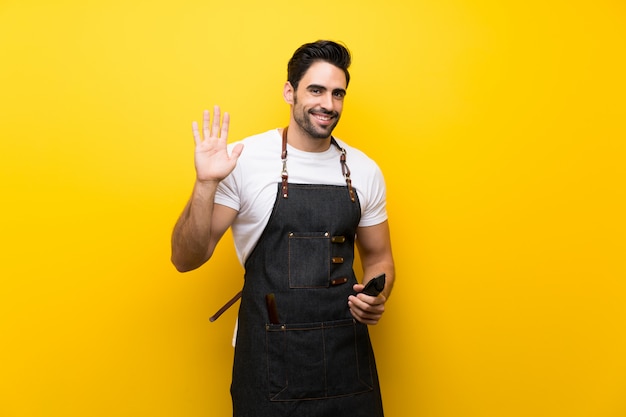 Young hairdresser man saluting with hand with happy expression