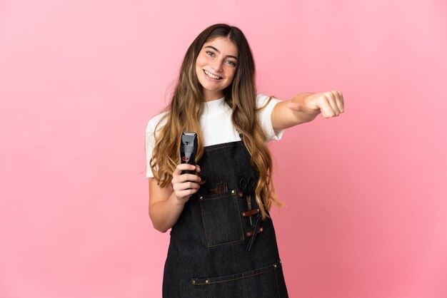 Молодая женщина-парикмахер изолирована на розовой стене, показывая большой палец вверх
