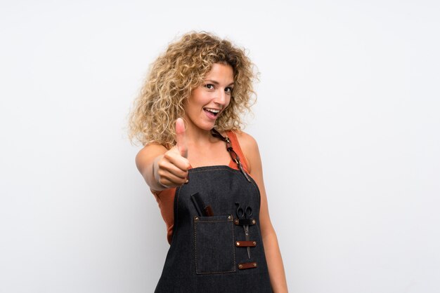 Young hairdresser woman over isolated wall with thumbs up because something good has happened