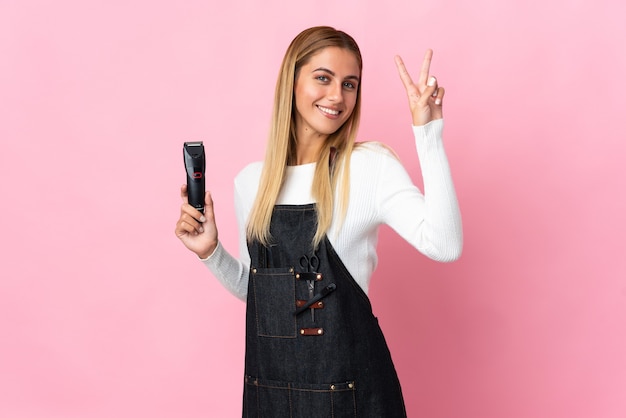 Young hairdresser woman on pink smiling and showing victory sign