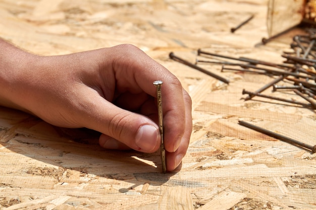 Photo young hand holding the nail to hammer it into plywood surface. repair work concept.