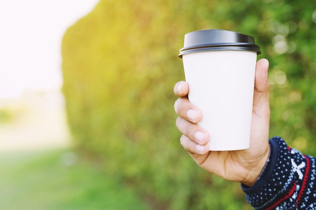 Young hand holding paper cup of take away drinking coffee on natural morning sunlight.