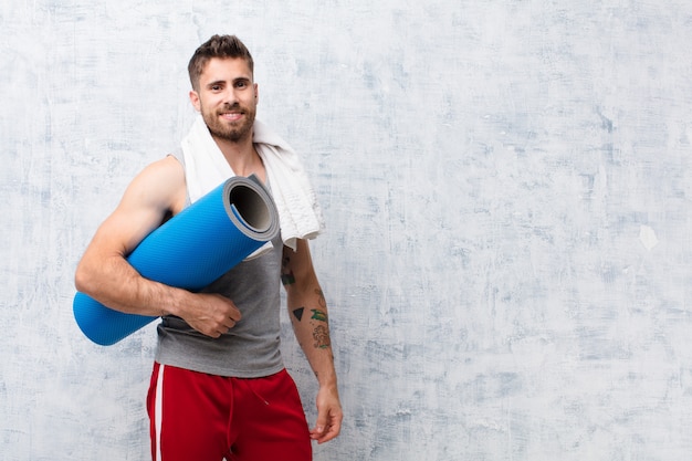 Young handosme man  against flat color wall with yoga mat. sport concept