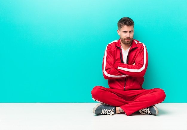 Young handosme man feeling displeased and disappointed, looking serious, annoyed and angry with crossed arms against flat color wall