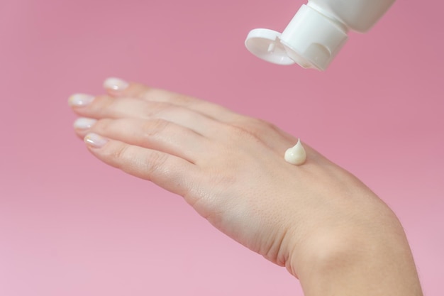 Young hands squeezing cream from tube on pink background for\
beauty or medicine products