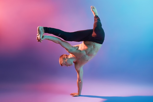 Фото Молодой красивый акробат или гимнаст тренируется, чтобы удерживать равновесие тела, стоя на одной руке, будучи босиком и топлес, касаясь его ноги, показывая свою силу.