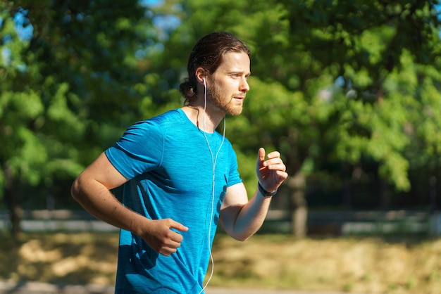 Young handsome active sportsman in blue shirt running on hot sunny day in nature