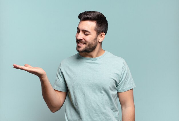 Young handsome adult man feeling happy and smiling casually, looking to an object or concept held on the hand on the side