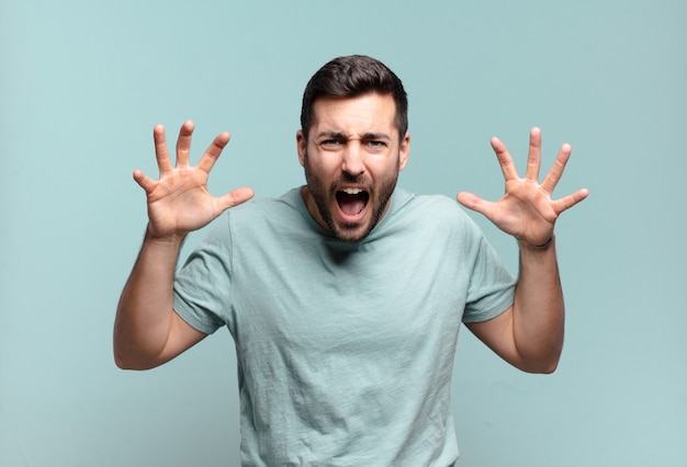 Young handsome adult man screaming in panic or anger, shocked, terrified or furious, with hands next to head