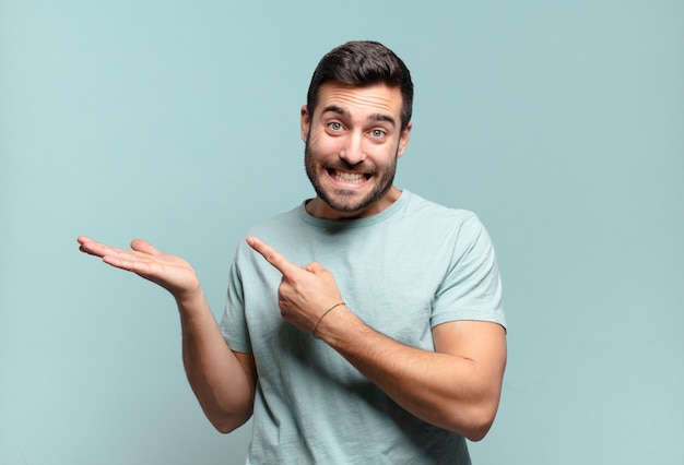 Young handsome adult man smiling cheerfully and pointing to copy space on palm on the side, showing or advertising an object