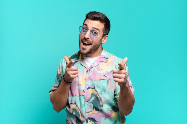 Young handsome adult man smiling with a positive, successful, happy attitude pointing to the front, making gun sign with hands