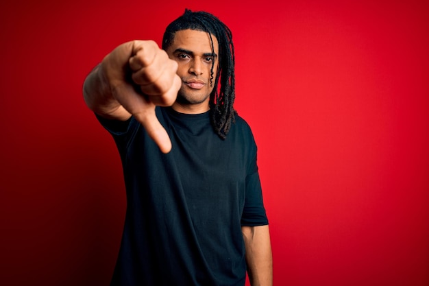 Young handsome african american afro man with dreadlocks wearing casual tshirt looking unhappy and angry showing rejection and negative with thumbs down gesture Bad expression