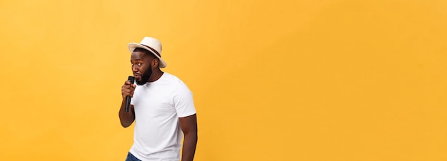 Young handsome african american boy singing emotional with microphone isolated on yellow background