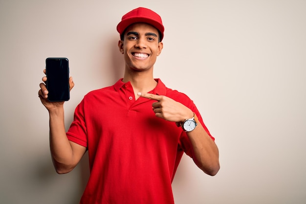 Young handsome african american delivery man holding smartphone showing screen app very happy pointing with hand and finger