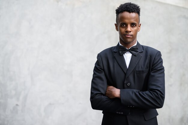 Young handsome African businessman wearing suit against concrete