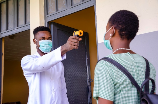 A young handsome african class teacher holding as thermometer to scan the temperature of his student before entering the classroom