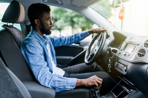 Giovane uomo africano bello cambiare marcia durante la guida di auto